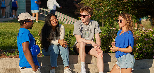 Four smiling students in GVSU apparel stand together outdoors on campus